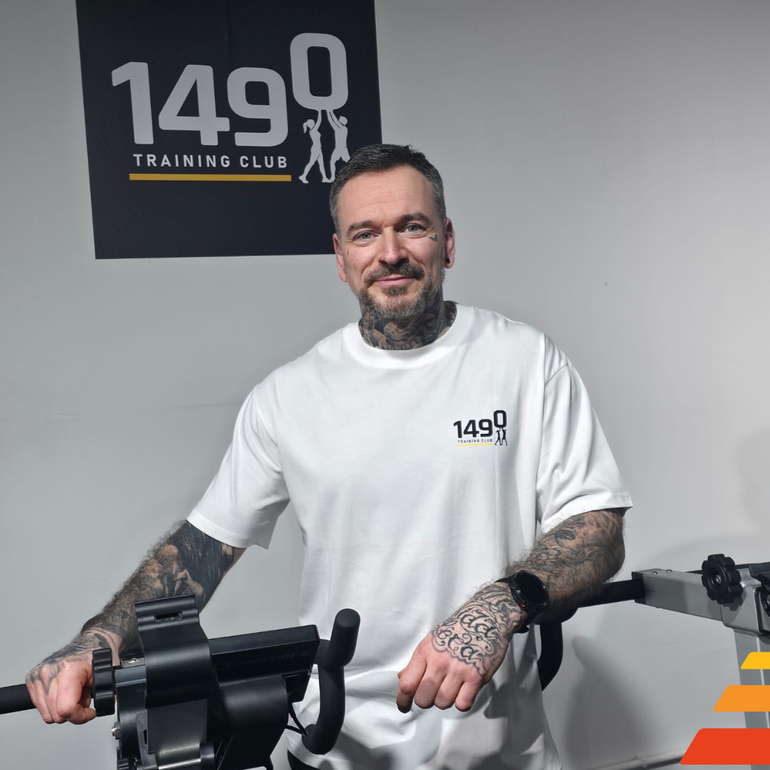 Portrait de Javier Luparello, head coach du 1490 Training Club, bras croisés, tatouages visibles, sur fond graphique aux couleurs du club.